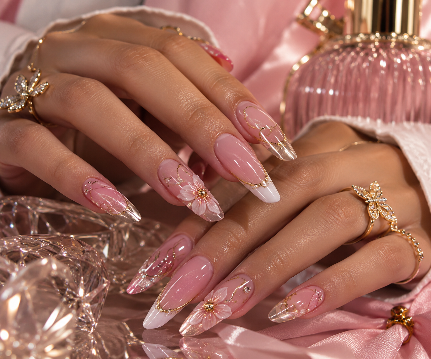 Mãos femininas com unhas rosa e douradas, flores delicadas e anéis de borboleta